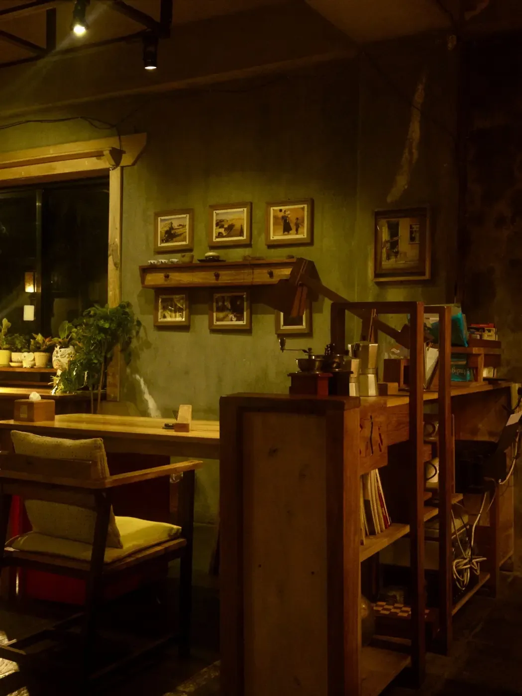 Café am Abend: warmes Licht, Holzmöbel, Pflanzen am Fenster und eine Handmühle auf der Theke